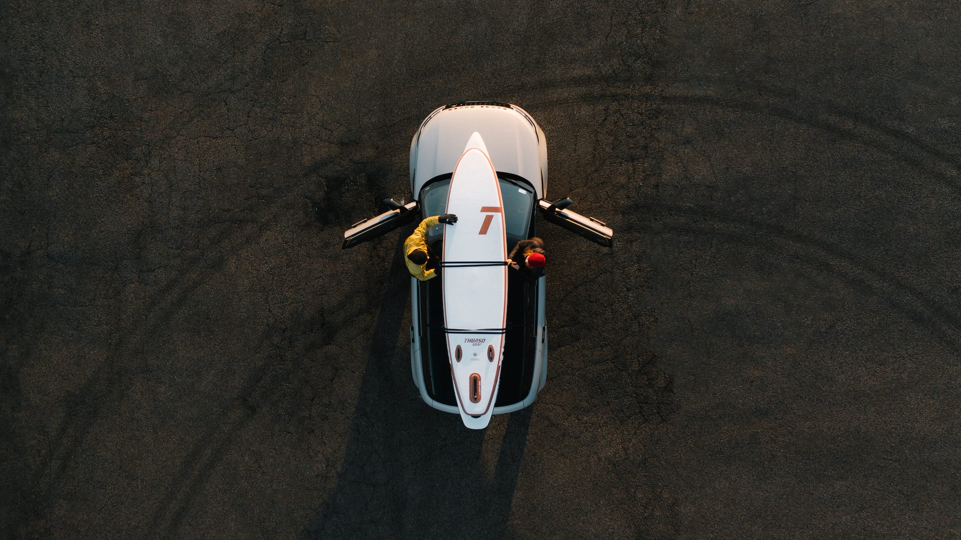 Bird's-eye view of two people securing paddleboards to the roof of a car