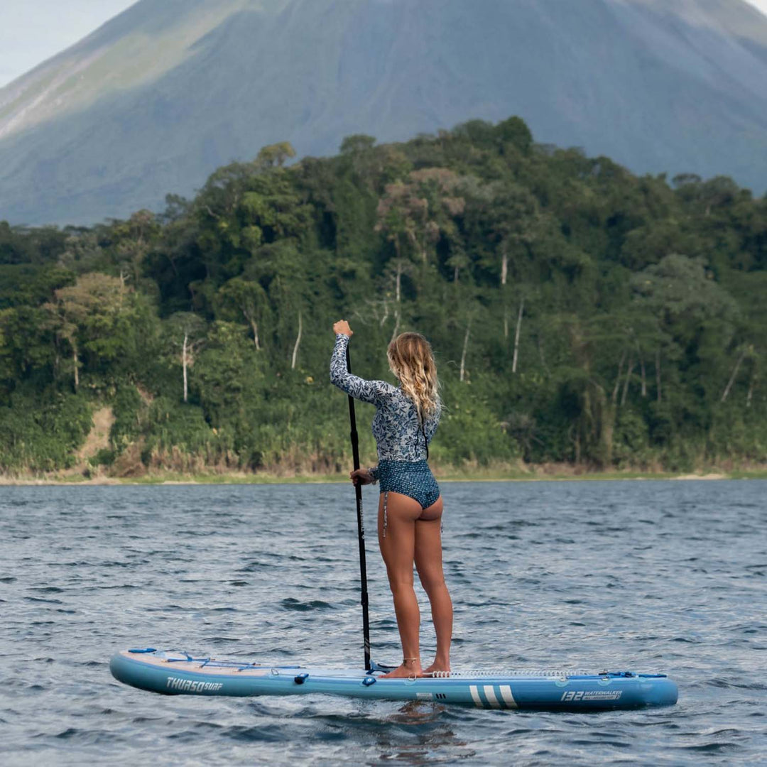 A woman stand on Thurso Surf Waterwalker 132 all-around SUP Dusk on Lake