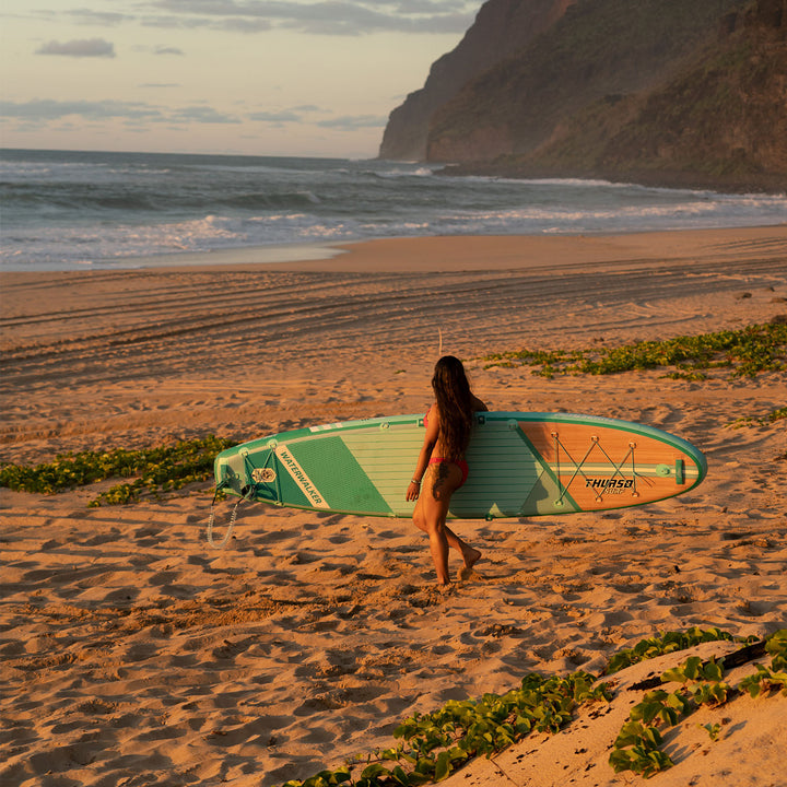 A woman standing on the beach with an thurso surf inflatable stand up board