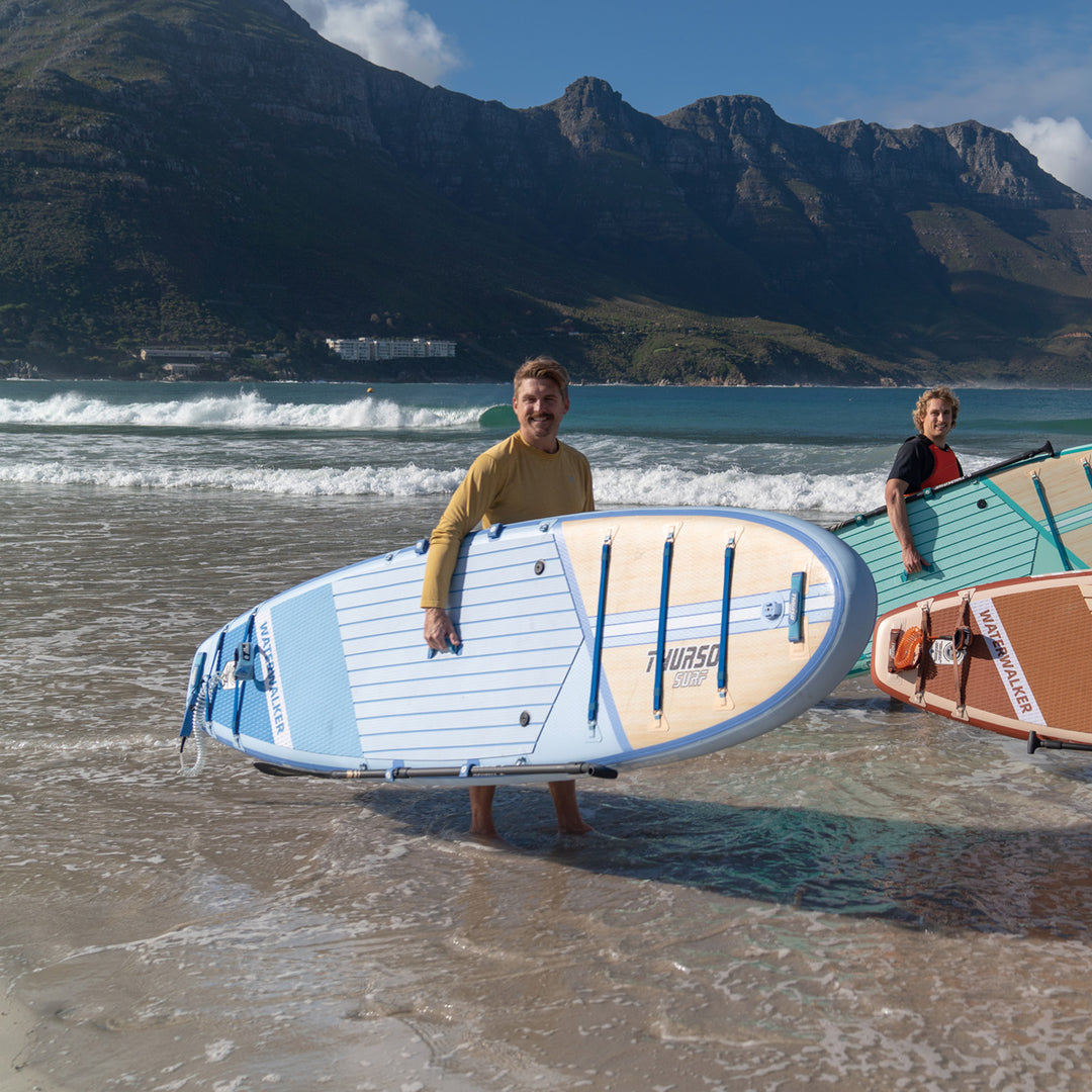 A man with dusk paddleboard on a beach with mountains in the background
