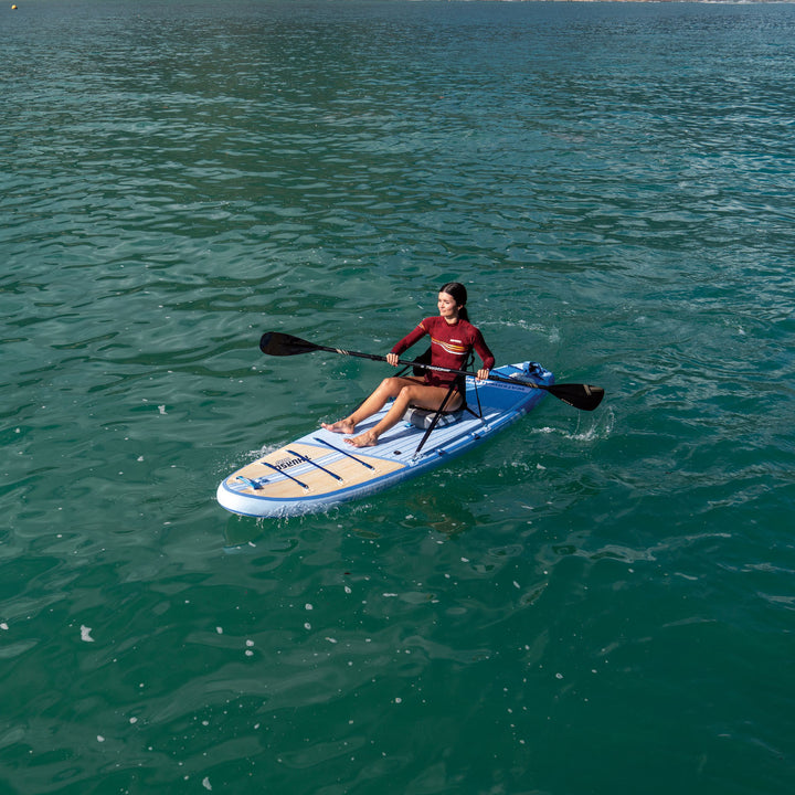 Person paddleboarding on a dusk and white board in the ocean.