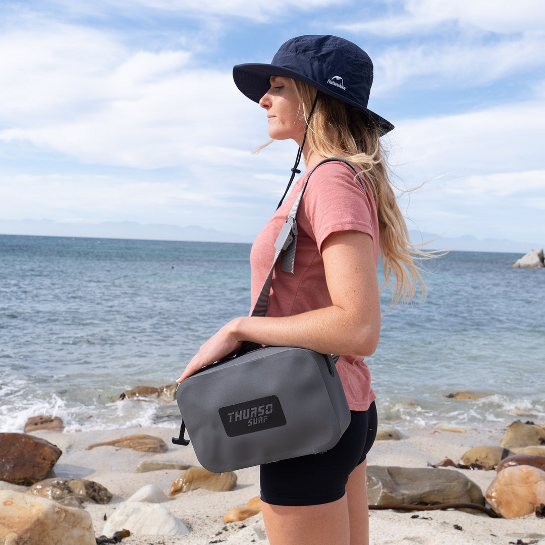 Woman holding a slate bag with 'Thursd' branding on a beach