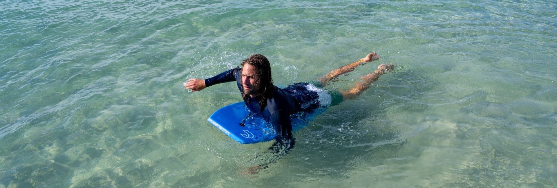 Person in a wetsuit with a blue bodyboard in shallow water