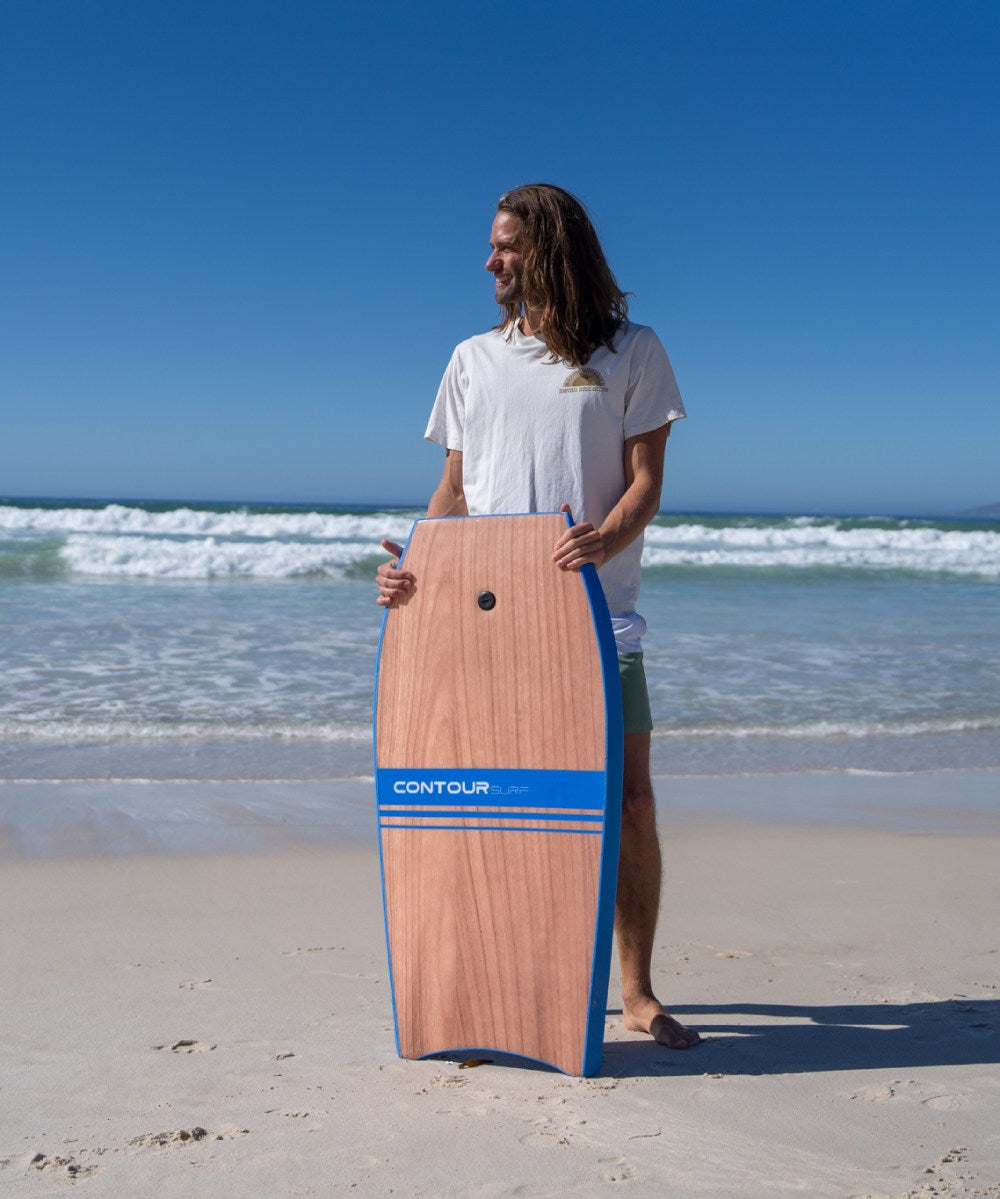 Person holding a wooden bodyboard with blue accents on a beach