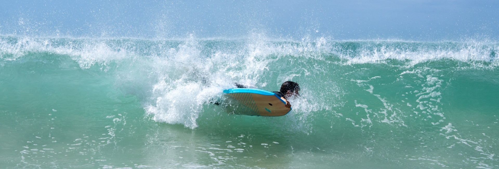 Person surfing on a wave with clear blue sky