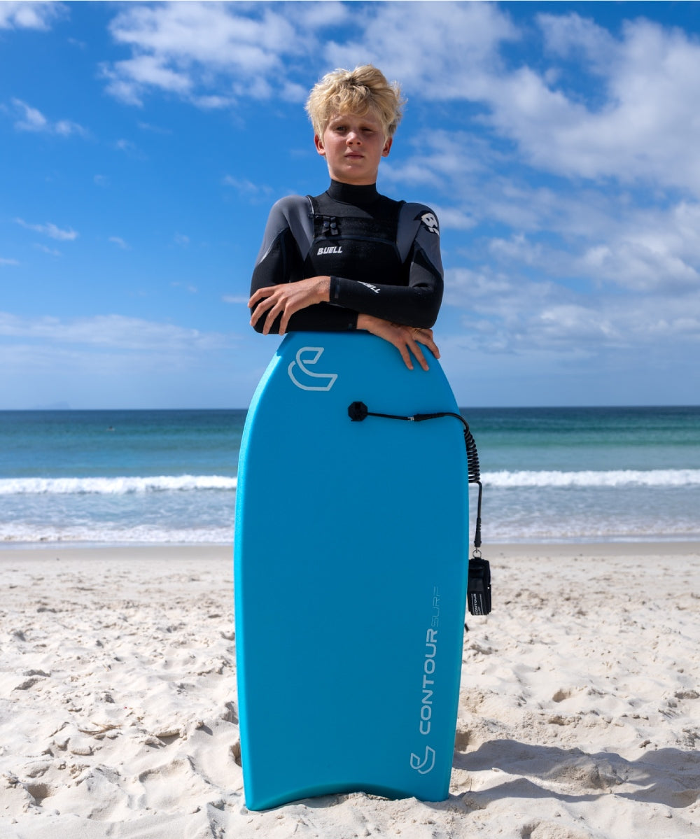 Person holding a blue bodyboard on a sandy beach with ocean and sky in the background