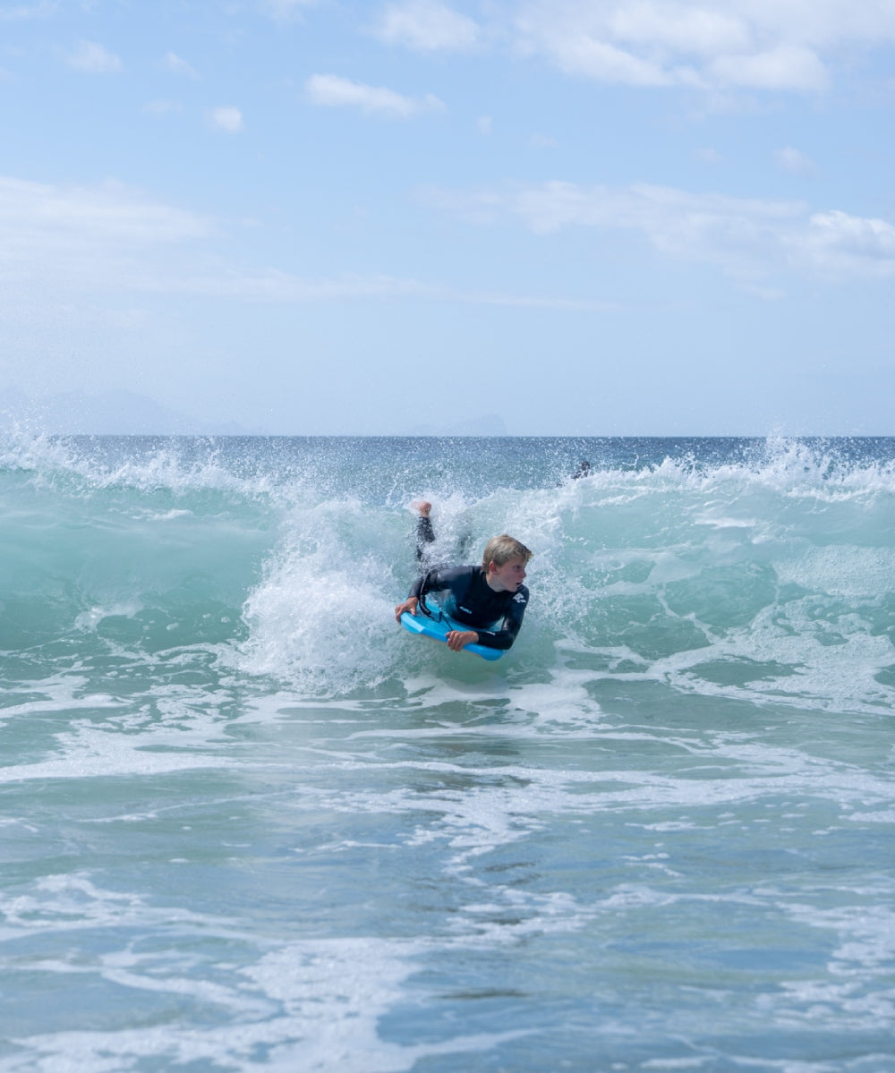Person surfing on a wave in the ocean with clear blue sky.