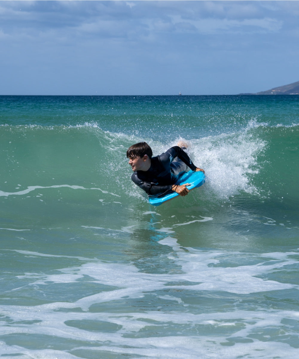 Person surfing on a blue bodyboard in the ocean with a clear sky.